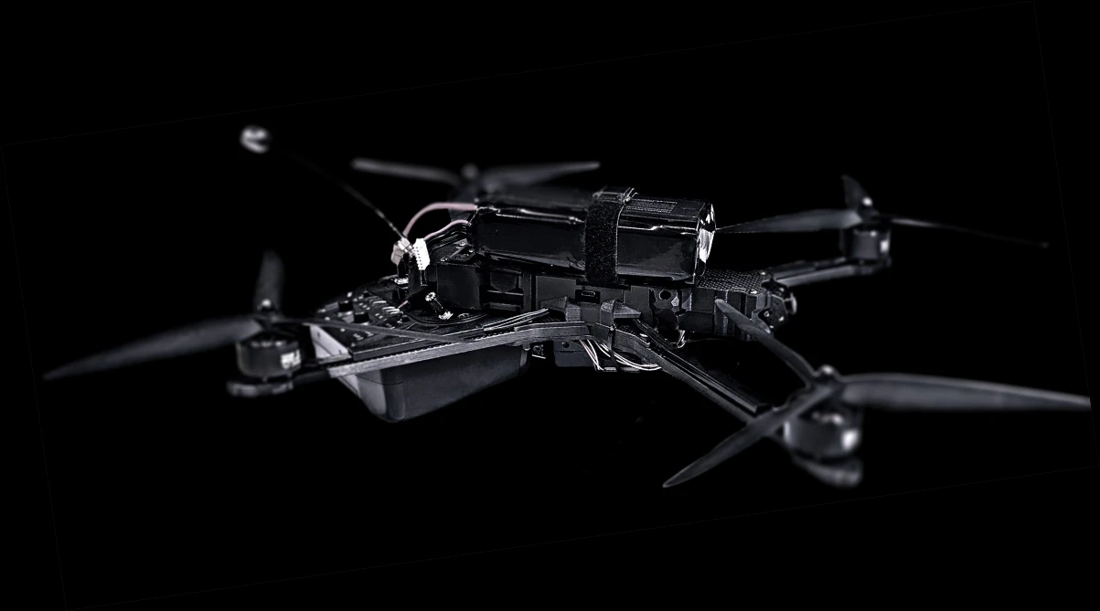 Black quadcopter drone with four propellers and visible wiring, shown against a dark background.